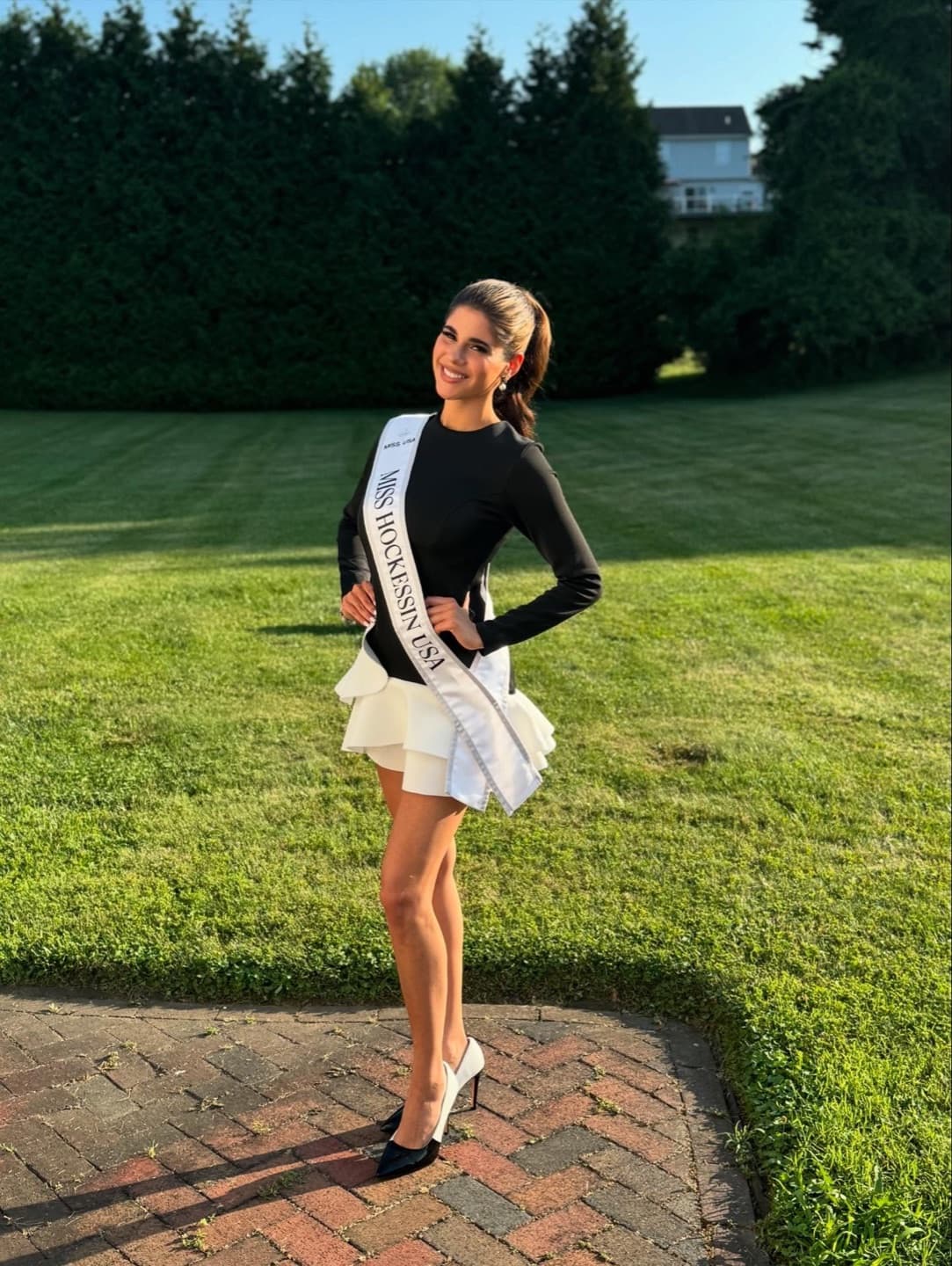 Julia Hatoum wearing a pageant sash outdoors on a sunlit lawn